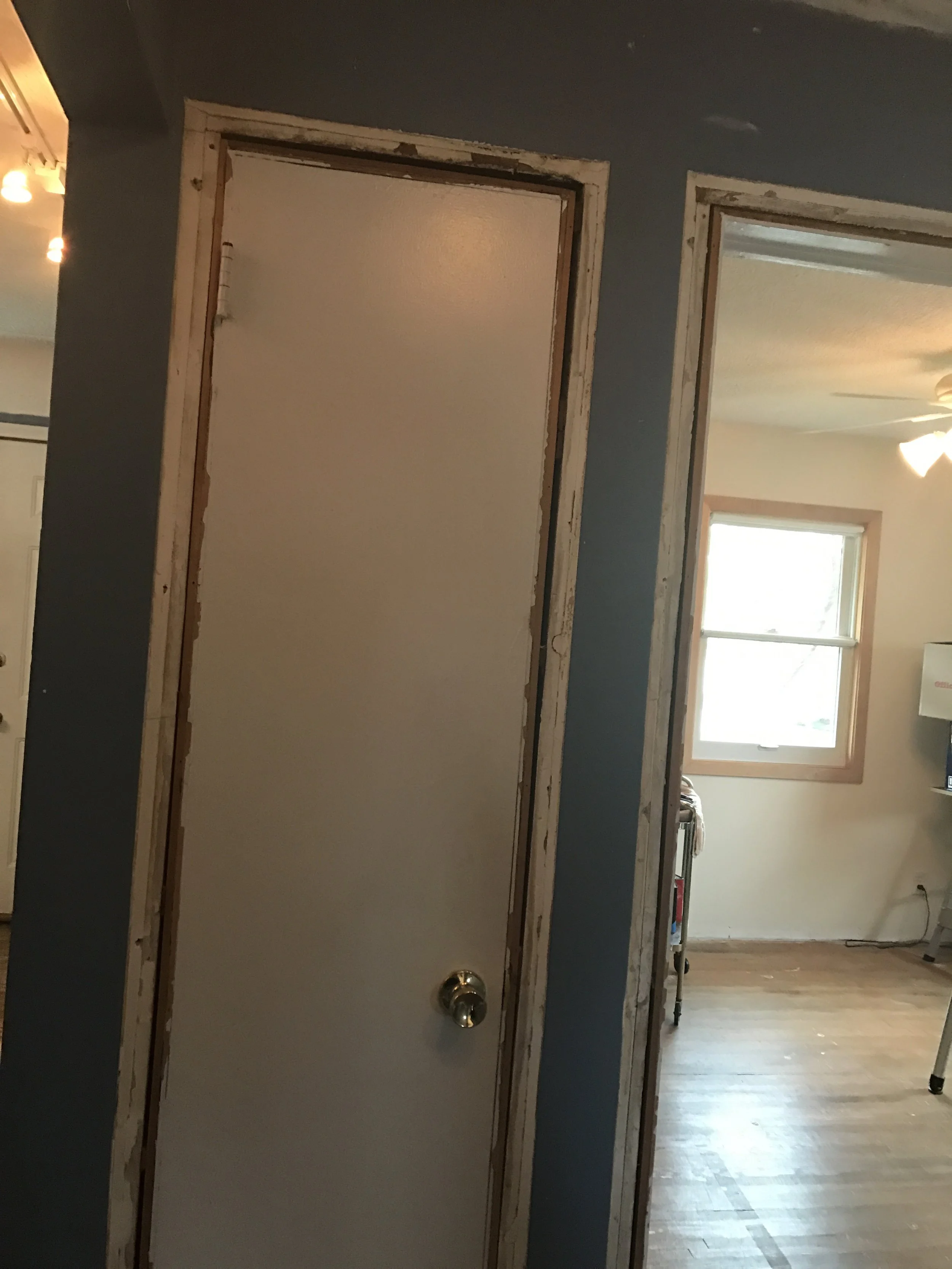 Hallway under renovation with unfinished door frames, blue wall and wood floor