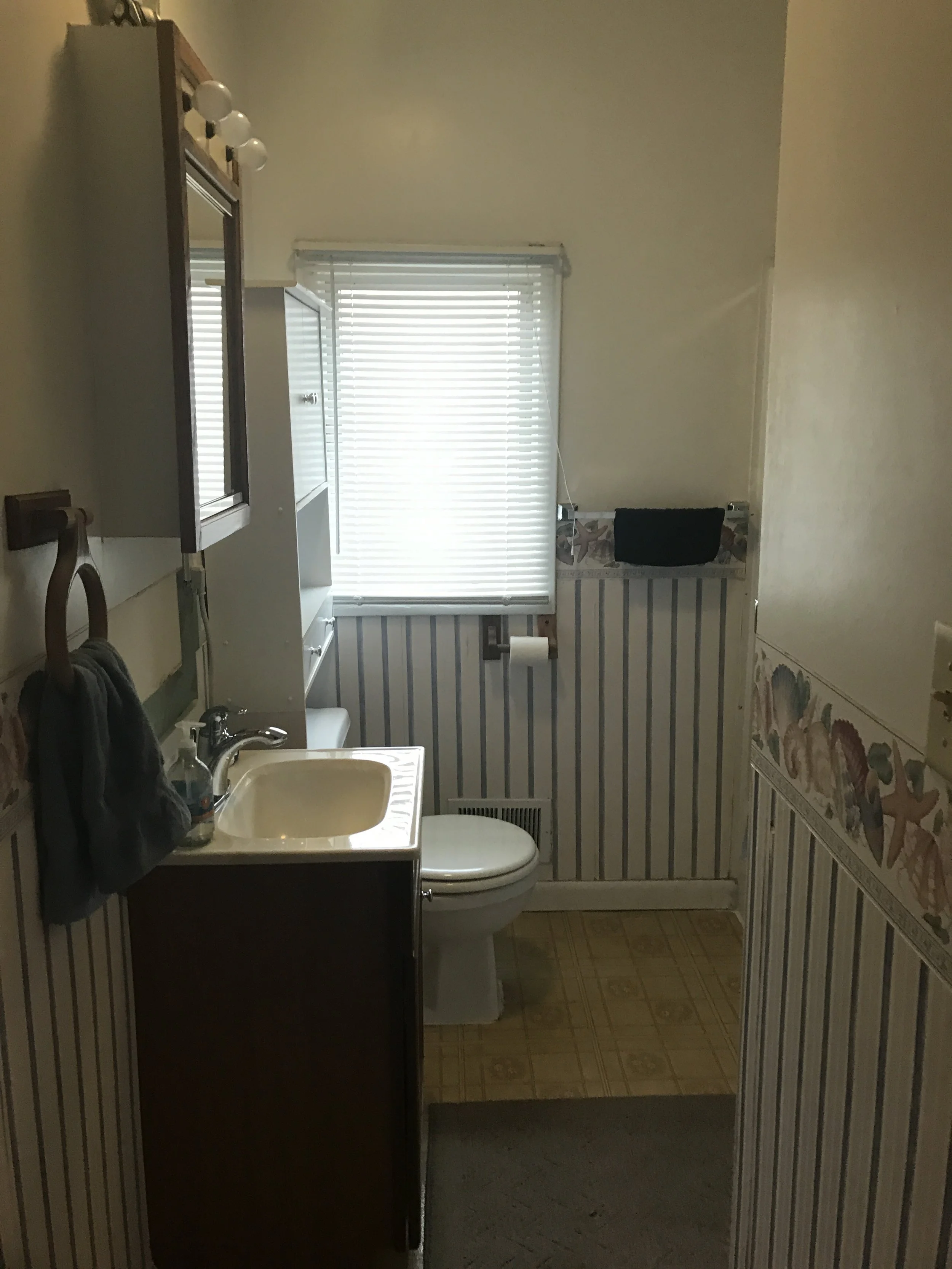 Small bathroom with striped wallpaper, white toilet, dark wood vanity and window blinds