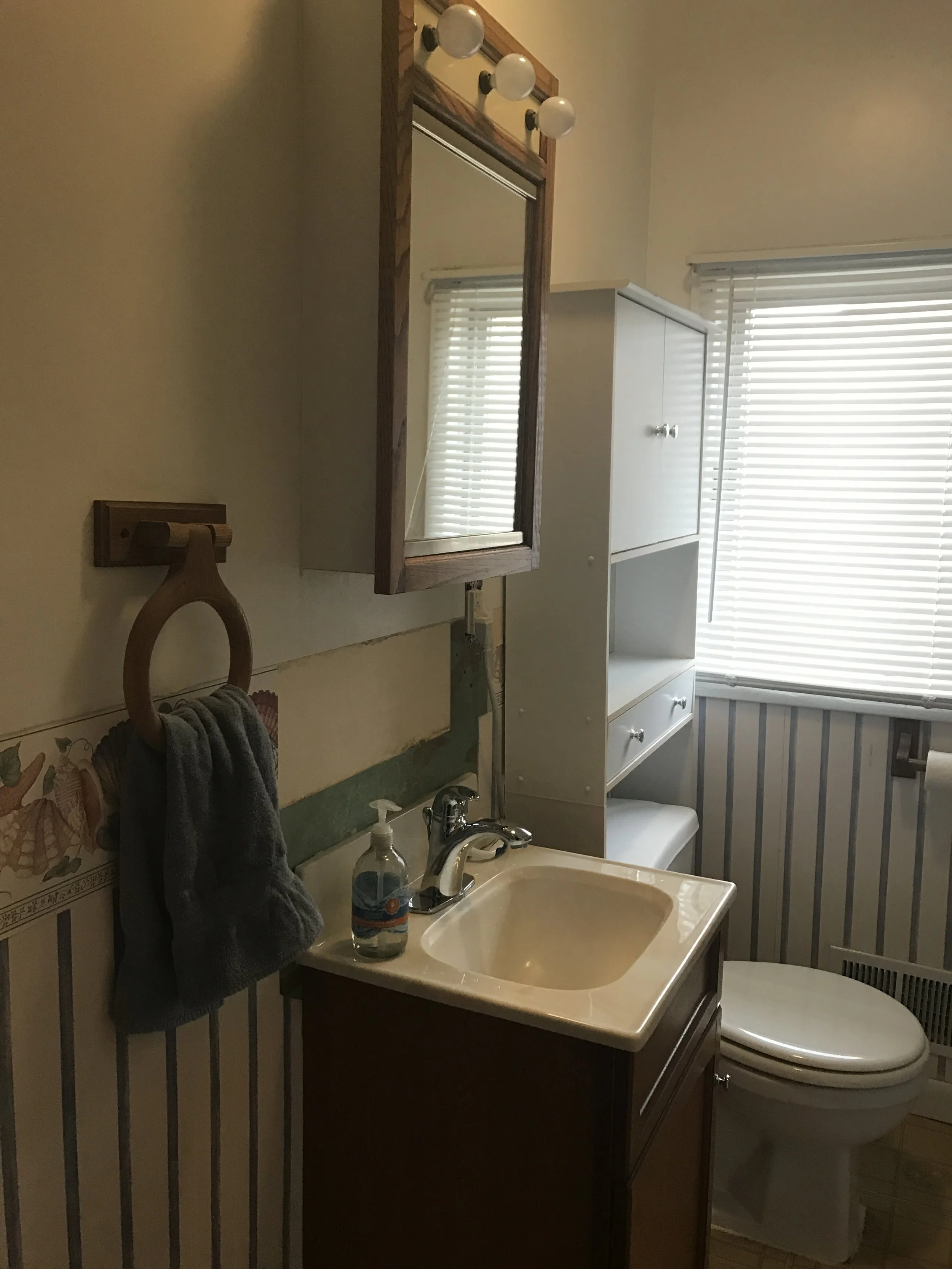 Bathroom close-up with wood-framed mirror, light fixture, sink and striped wallpaper in muted neutrals