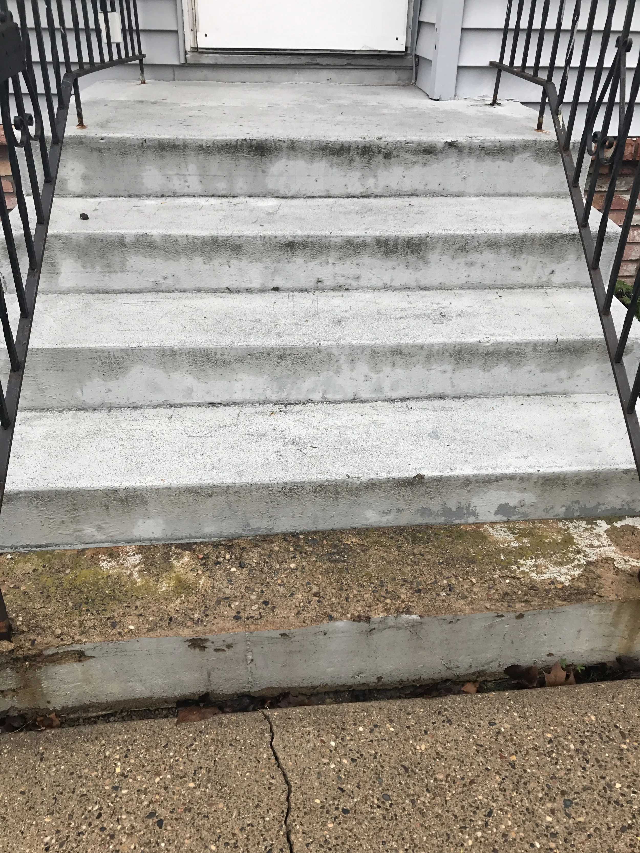 Outdoor concrete steps with black metal railings leading to a white door in muted neutrals