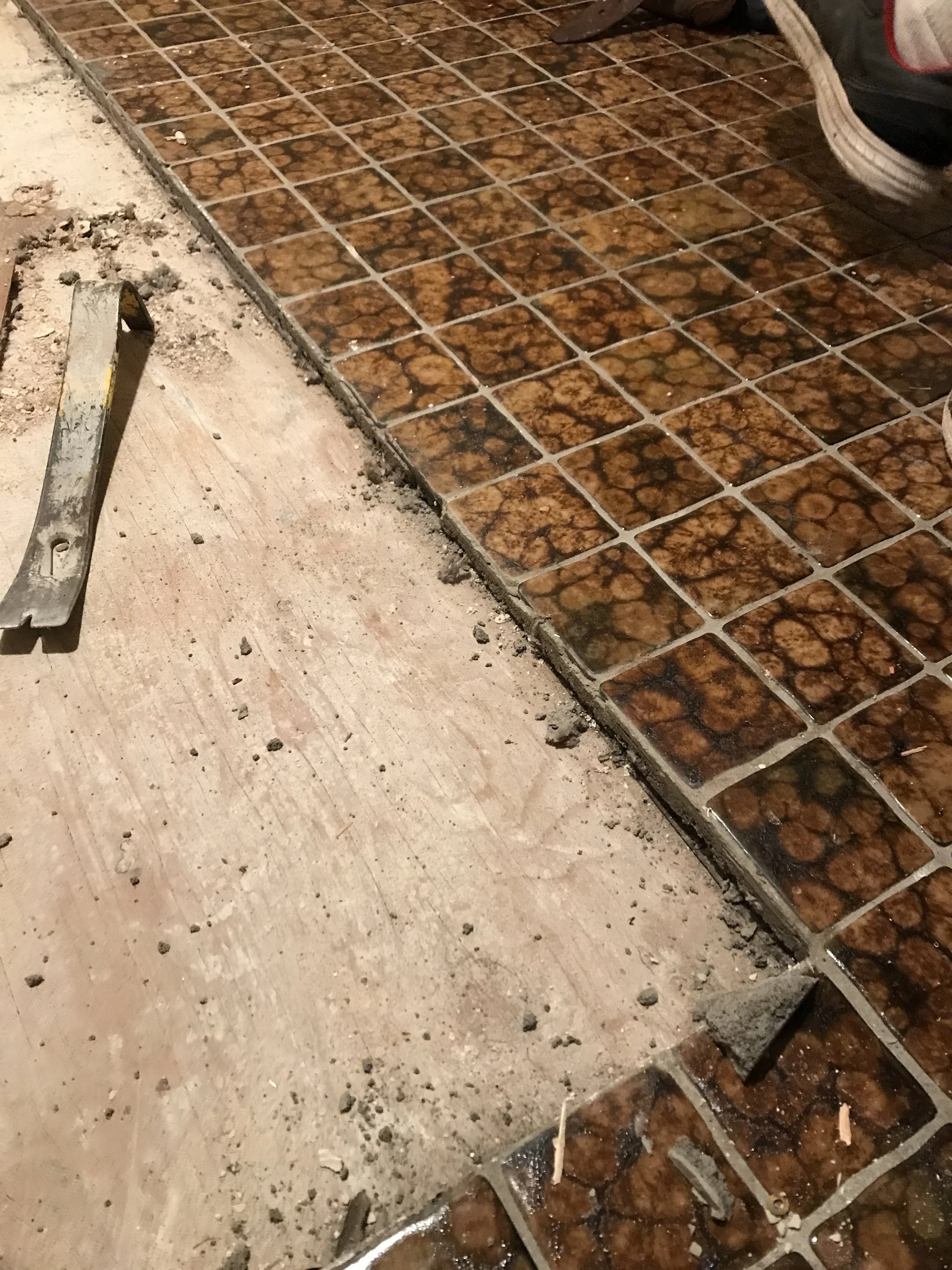 Close-up of old mottled brown tile flooring being removed next to bare subfloor