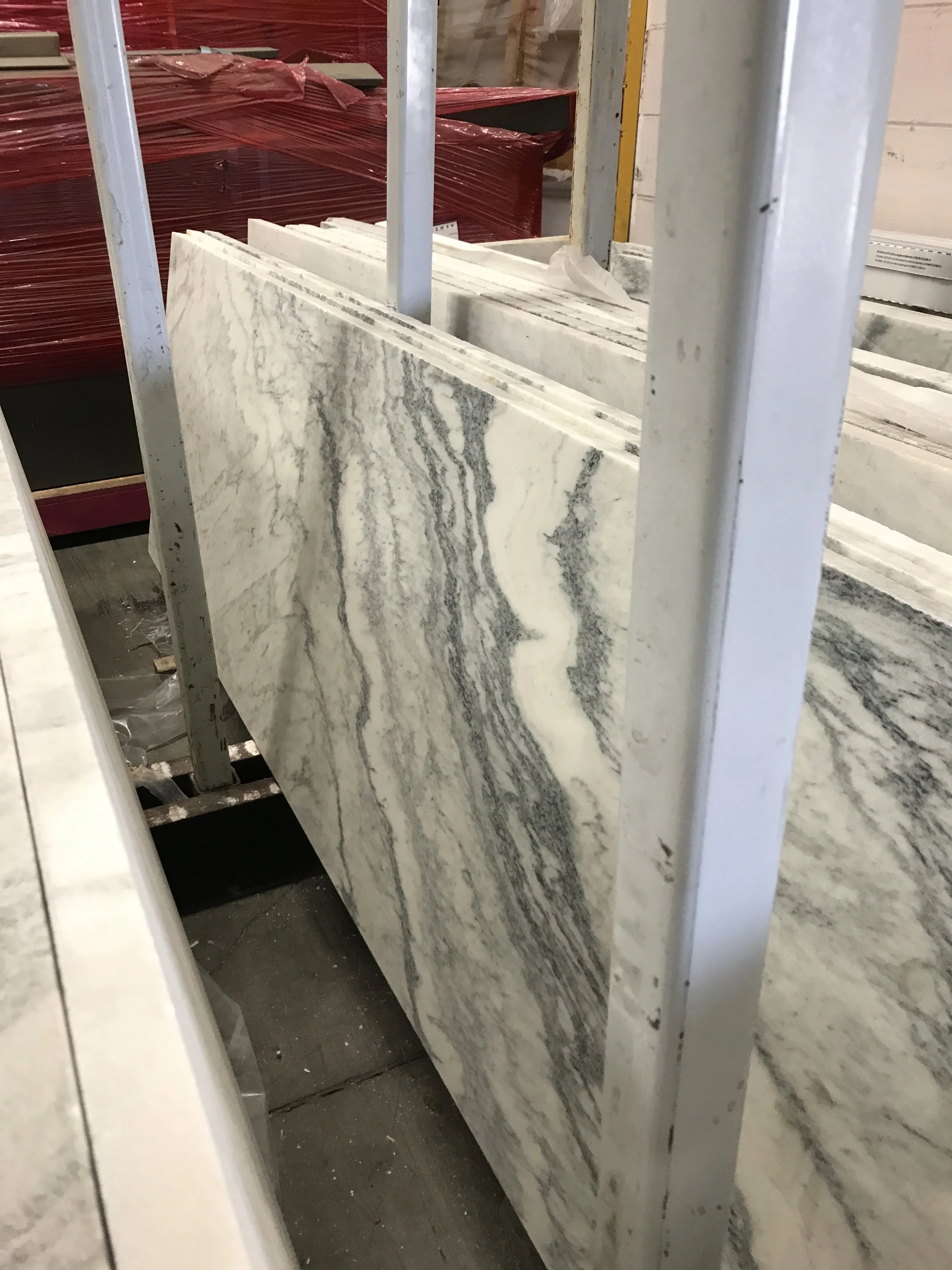 Large white and gray veined stone slabs stored upright on a metal rack in a warehouse, neutral and industrial mood