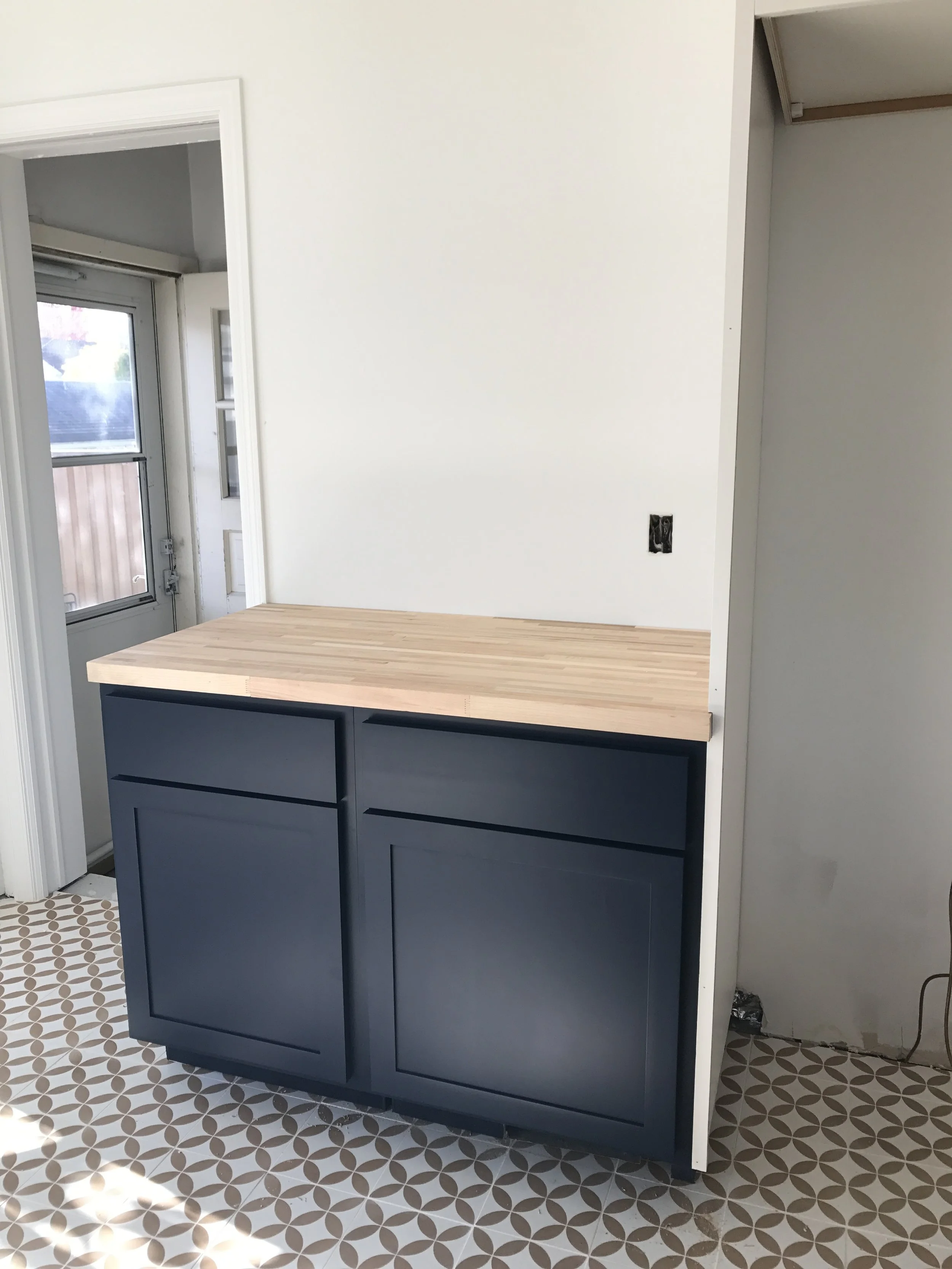 Small kitchen island with dark blue cabinet doors and a light wood countertop beside patterned tile