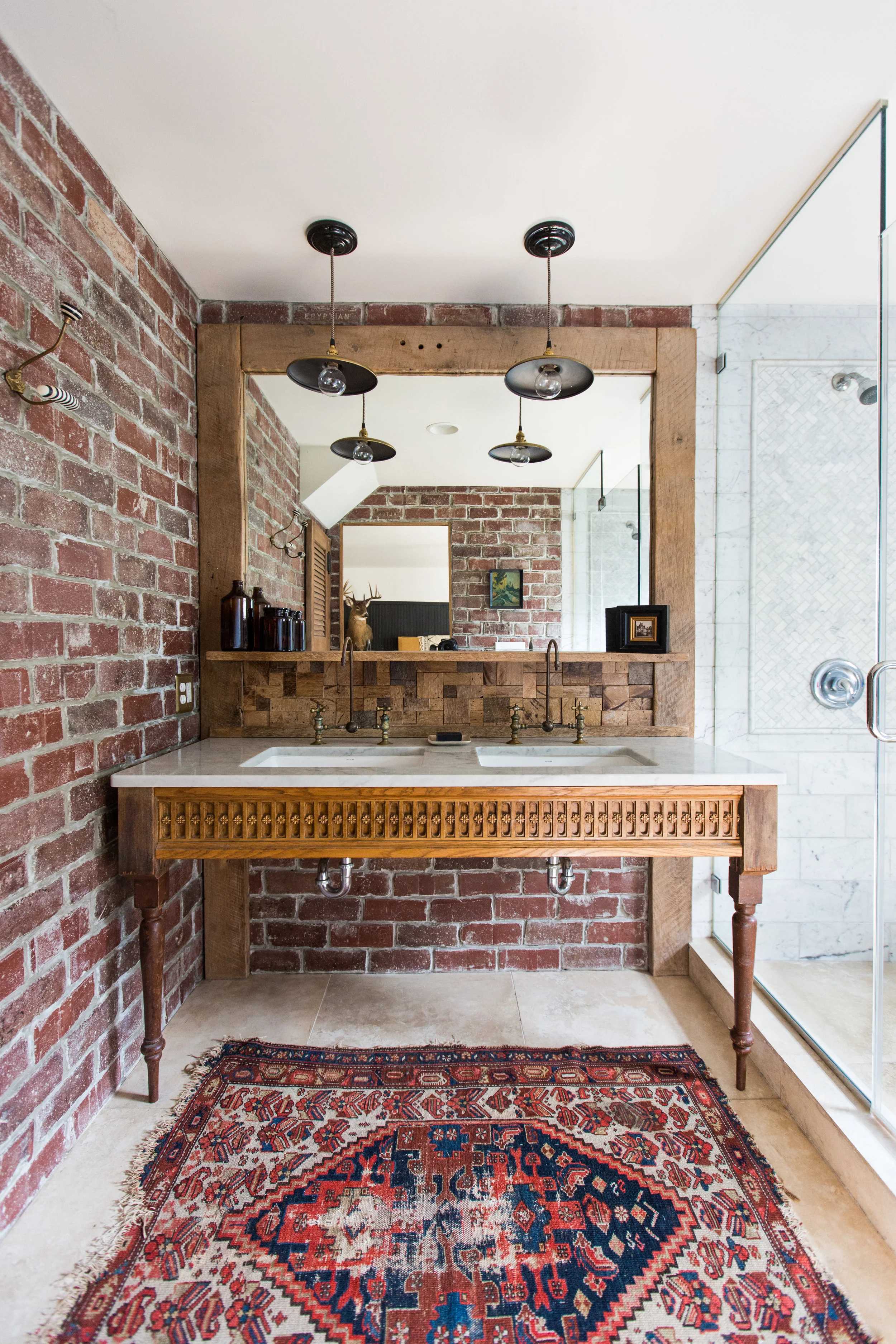 Bathroom vanity with exposed brick, wood-framed mirror, double sinks and warm pendant lights in soft cream and brick tones